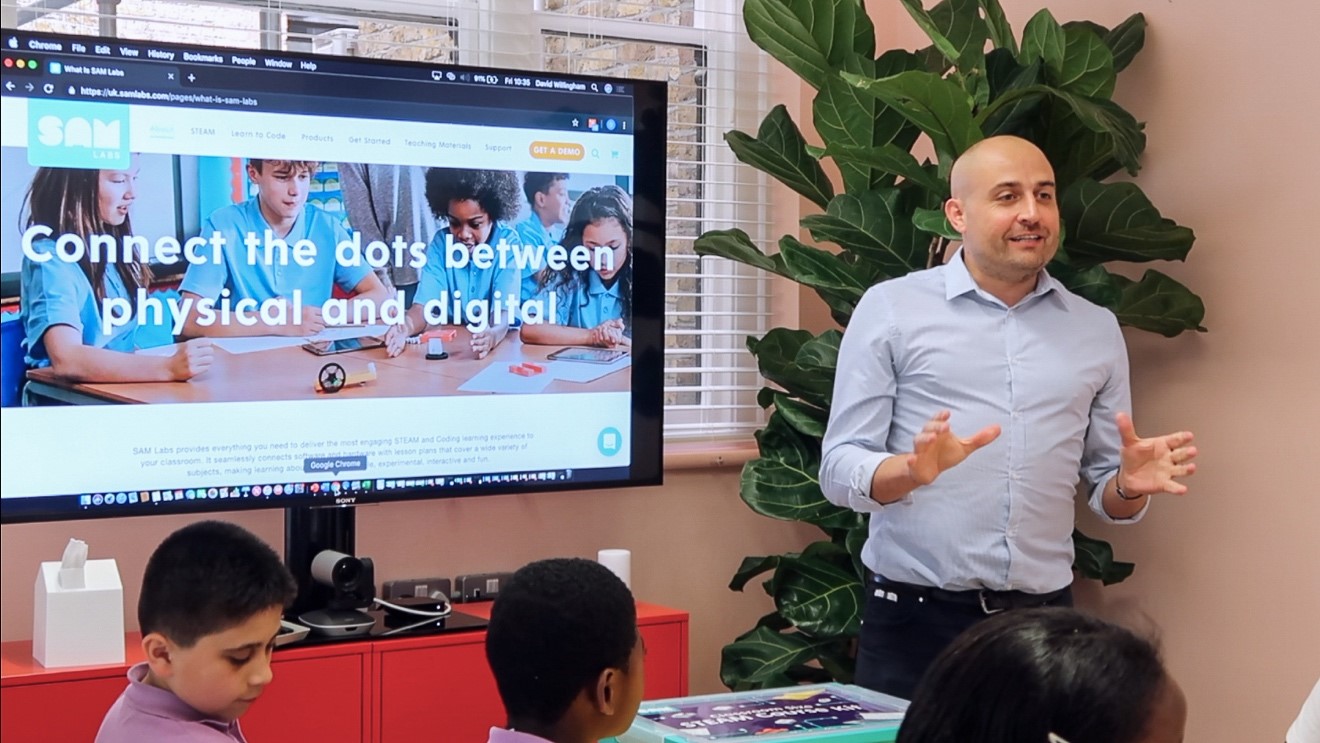 Man presenting to children about jobs in tech, the screen reads Connecting the dots between physical and digital